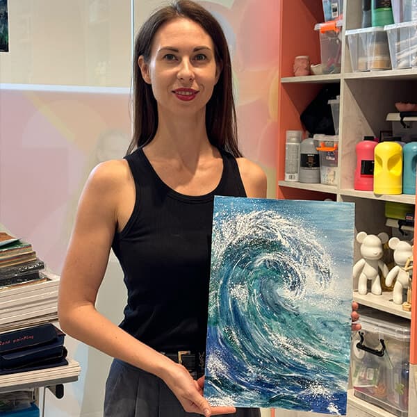 Adult student holding her finished acrylic wave painting after a class in Dubai